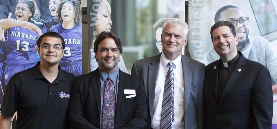 Student, Dr. Frascatore, Dr. Ireland and Father Maher standing in front of banners.