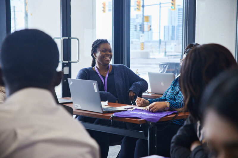 Student laughing sitting at a table with a computer on it