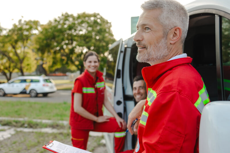 A group of emergency medical personnel work near an ambulance during a daytime response. The team appears engaged and motivated, exemplifying teamwork, healthcare, and emergency response preparedness in an outdoor setting.