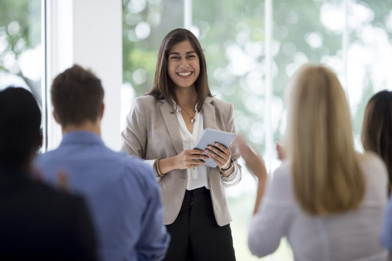 A multi-ethnic group of business professionals are listening to a presentation from a colleague during a meeting in the boardroom. They are clapping after a presentation.